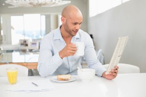 Concentrated young man drinking coffee while reading newspaper a